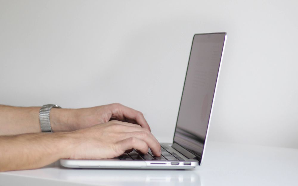A person using a slim laptop on a clean white table.