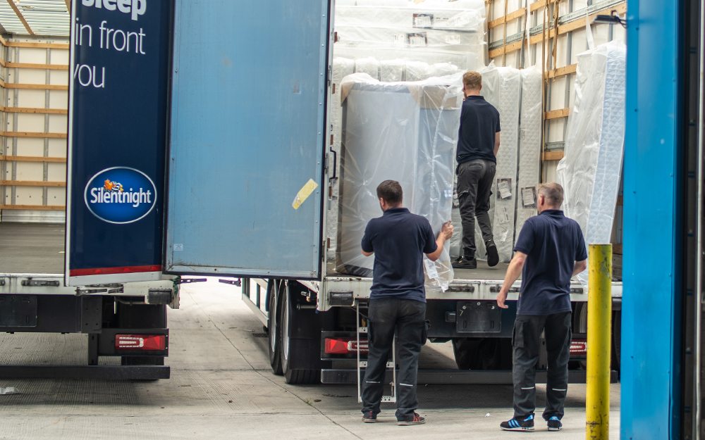 Three Mattress Online staff loading a plastic-covered mattress into a delivery van